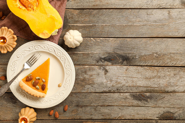 Plate with piece of delicious pumpkin tart and almond on wooden background - Photo, Image