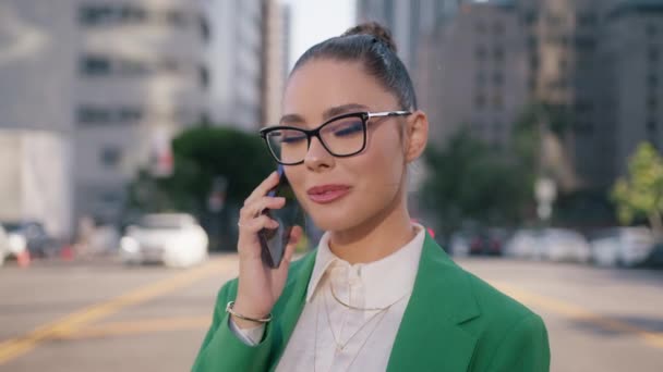 Krásná pozitivní žena ve stylových brýlích mluví po telefonu ve finanční čtvrti. Úspěšný manažer s úsměvem při používání smartphonu. Usmívající se podnikatelka v elegantním oblečení v moderním městě - Záběry, video