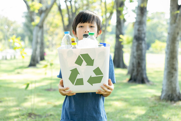 Veselý mladý asijský chlapec držící popelnici s recyklačními symboly na denním přírodním zeleném parku, podporující recyklaci odpadu, snižující a opětovně využívající povzbuzení k ekologickému udržitelnému povědomí pro budoucí generaci. Gyre - Fotografie, Obrázek
