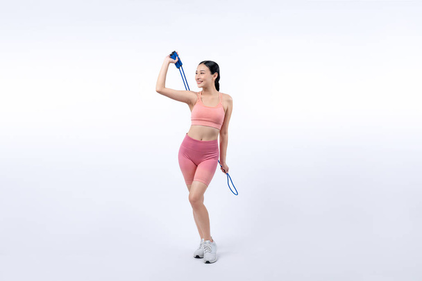 Jeune femme asiatique énergique en tenue de sport avec robe sautant ou sautant posant portrait en studio tourné sur fond isolé. Outil d'exercice cardio et mode de vie sain de soins du corps. Vigoureux - Photo, image