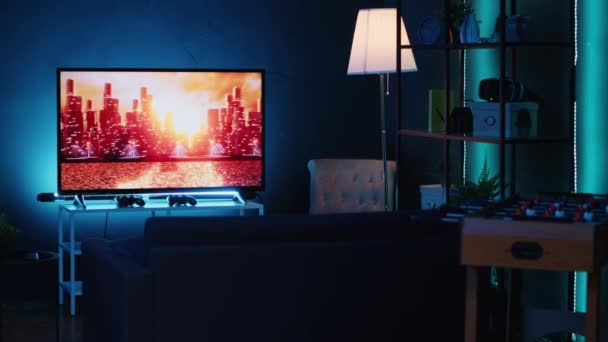 Prázdný stylový neon osvětlený interiér domácího studia osvětlený v noci neonovými světly a malbami zdobícími stěny. Moderní byt s TV běží v pozadí na zpravodajském kanálu vysílání - Záběry, video