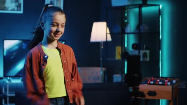 Schwenkbild eines charismatischen kleinen Mädchens, das mittels Handy auf Stativ ein trendiges Tanzvideo für die sozialen Medien aufnimmt und damit das Publikum unterhält. Internet-Star Gen z filmt mit Handy - Filmmaterial, Video