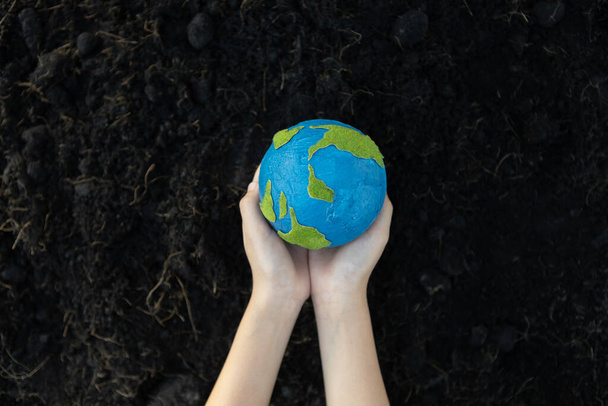 Young boys hand holding planet Earth globe on fertile soil background as Earth day to save this planet with ESG principle and environment friendly energy for brighter future. Gyre - Photo, Image