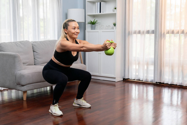 Спортивная и спортивная старшая женщина, участвующая в тренировках в день ног с мячом чайника и приседания на дому, как концепция здорового здорового образа жизни тела после выхода на пенсию. Clout - Фото, изображение