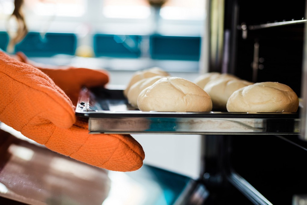 Bäckerhände mit Topflappen neben Blech  - Foto, Bild