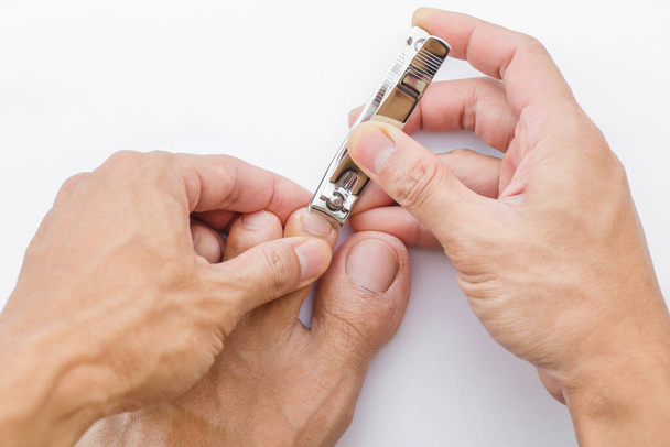El hombre se corta las uñas con pinzas sobre un fondo blanco. Ilustración del cuidado de las uñas Por su buena higiene. - Foto, Imagen
