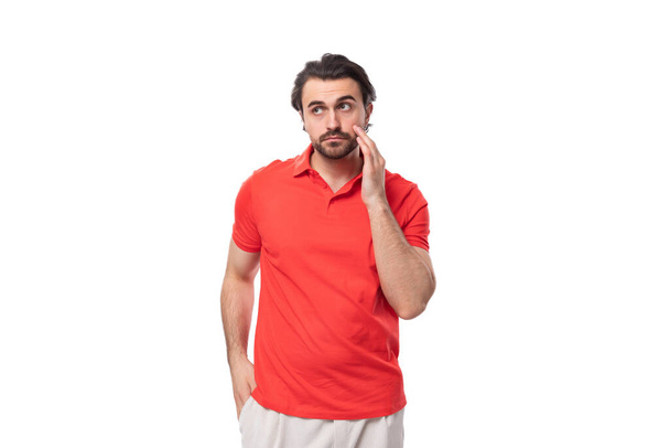 jovem morena homem com barba está vestido com uma camiseta vermelha com um mockup em um fundo branco com espaço de cópia. vestuário corporativo. - Foto, Imagem