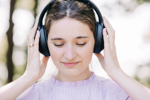 Capturée en gros plan, une femme s'immerge dans la musique à travers ses écouteurs, symbole de liberté et de bonheur dans un décor extérieur. Ce cadre vert serein améliore l'expérience, parfait - Photo, image