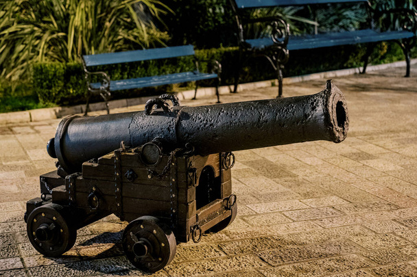 Ancien canon en bronze sur un chariot en bois avec roues se dresse sur les pavés près du banc. Photo de haute qualité - Photo, image