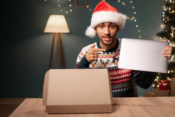 Mannelijke vlogger in Santa hoed op zoek naar camera filmen clip van unboxing internet order. Arabische klant ontvangt pakket geven positieve feedback. Kopieerruimte - Foto, afbeelding