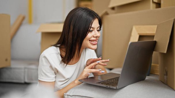Молода біла жінка використовує ноутбук, сидячи на підлозі в новому будинку
 - Фото, зображення