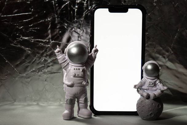 Plastic speelgoed figuur astronaut met mobiele telefoon wit scherm voor uw advertentie Kopieer ruimte. Concept van reizen buiten de aarde, particuliere ruimtevaarder commerciële vluchten. Ruimtemissies en duurzaamheid - Foto, afbeelding