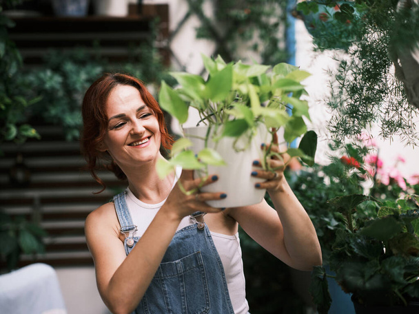 Een vrouw tuiniert planten op een balkon, voedt groen leven in een stedelijke omgeving - Foto, afbeelding