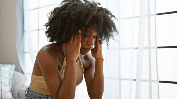 Donna afroamericana che soffre di mal di testa seduta sul divano di casa - Foto, immagini