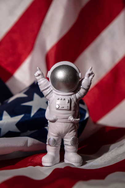 Plastic toy figure astronaut on American flag background Copy space. 50th Anniversary of USA Landing on The Moon Concept of out of earth travel, private spaceman commercial flights. Space missions and Sustainability - 写真・画像