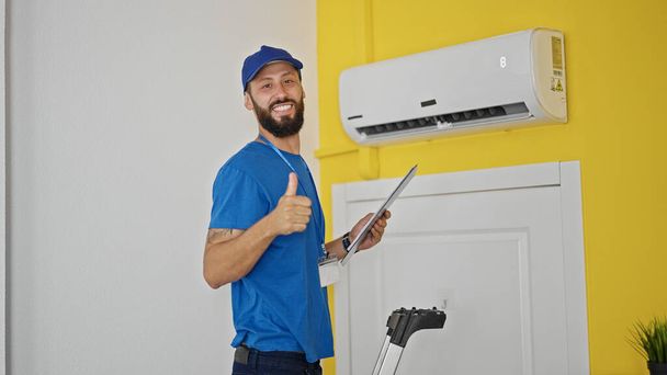 Νεαρός Ισπανός τεχνικός επισκευάζει κλιματιστικά κάνοντας χειρονομίες στο σπίτι - Φωτογραφία, εικόνα