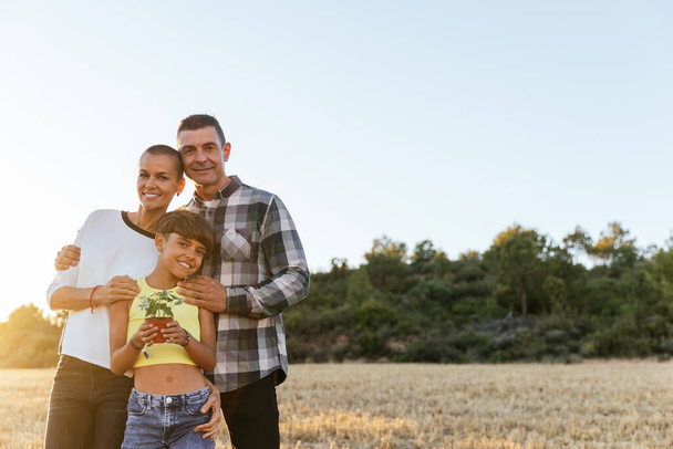 Liebevolle dreiköpfige Familie steht in einer wunderschönen ländlichen Landschaft, umarmt von der Freude und dem Glück des Zusammenseins bei Sonnenuntergang. - Foto, Bild