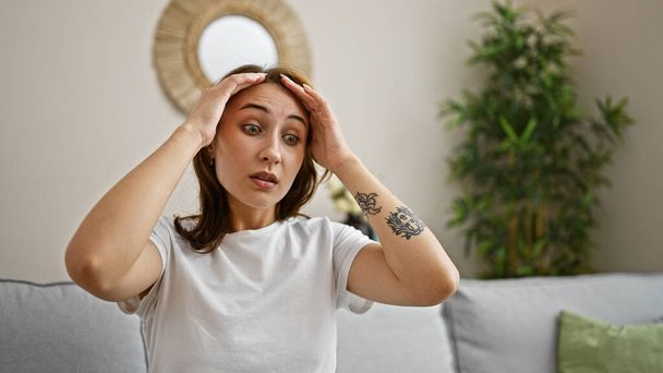 Молодая женщина страдает от головной боли, сидя дома на диване - Фото, изображение
