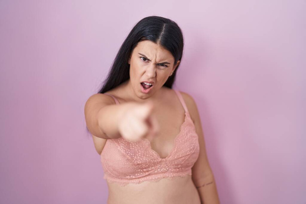 Junge hispanische Frau in rosa BH zeigt unzufrieden und frustriert in die Kamera, wütend und wütend auf dich  - Foto, Bild