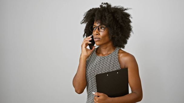 Femme afro-américaine ouvrière parlant sur smartphone tenant presse-papiers sur fond blanc isolé - Photo, image