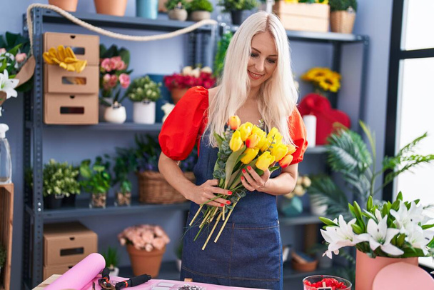 Молода блондинка-флорист тримає букет квітів у квітковому магазині
 - Фото, зображення