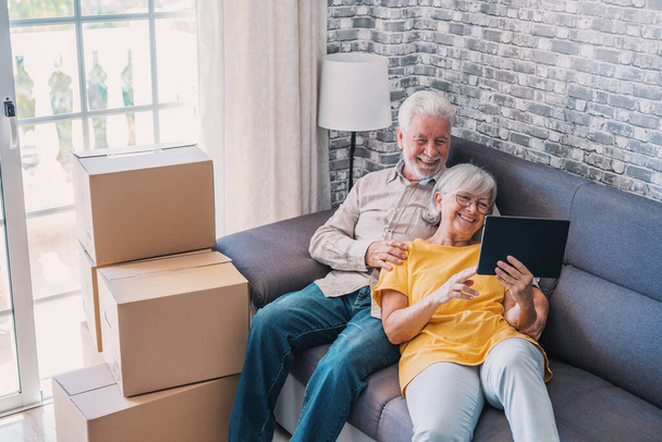 Szczęśliwa emerytowana para seniorów relaksująca się na sofie po przeprowadzce, dzieląca się tabletem, patrząca na ekran, śmiejąca się, dzwoniąca wideo, korzystająca z aplikacji online, serwis internetowy - Zdjęcie, obraz