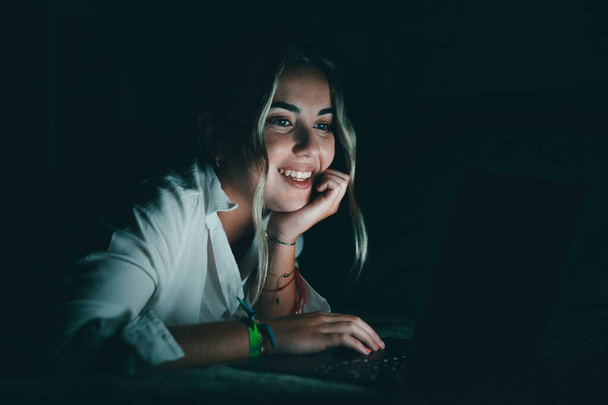 Lähikuva hymyilevä luottavainen valkoihoinen opiskelija käyttää kannettavaa tietokonetta yöllä sängyssä, työskentely, viimeistely projekti myöhään, määräaika, katsomalla tietokoneen näyttö, istuu makuuhuoneessa yliopiston kotitehtäviä - Valokuva, kuva