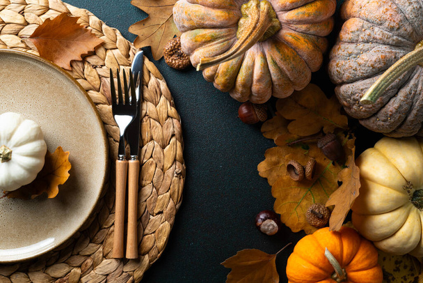 Cozy hygge table. Top view of plate and cutlery, pumpkins, autumn leaves on dark table. Autumn table setting. Festive Thanksgiving or Halloween background. Restaurant menu. Copy spac - Photo, Image