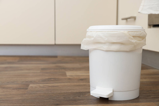 Trash can with bag on wooden floor on light background, space for text - Photo, Image