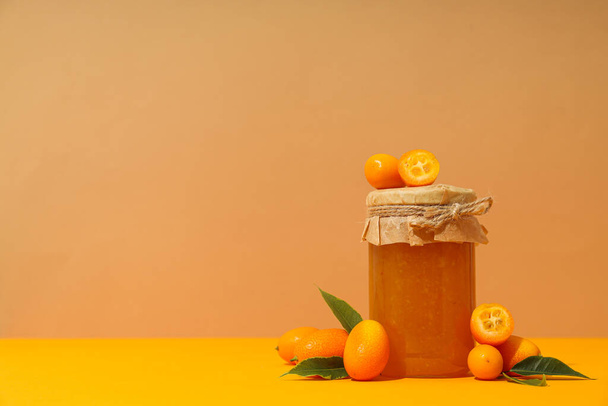 Kumquat and jar of jam on orange background, space for text - Photo, Image