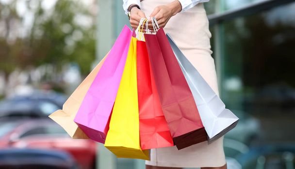 Donna in piedi vicino negozio di abbigliamento tenendo in mano mucchio di sacchetti di carta multicolore primo piano
 - Foto, immagini