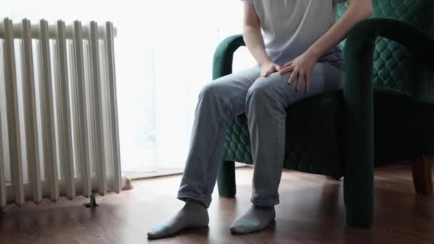 Close-up van een vrouw die in fluwelen fauteuil zit en haar been trillend wrijft van stress. Concept van zenuwstoornis en OCD. - Video