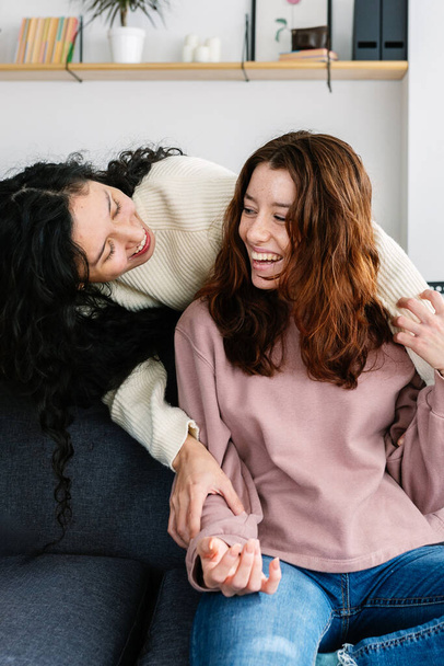 Vertical shot of young female friends having fun hugging each other at home. Teenage girls enjoying time together. Friendship concept. - Photo, Image