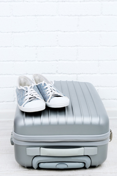 Gray suitcase with male shoes on floor on brick wall background - Foto, Bild