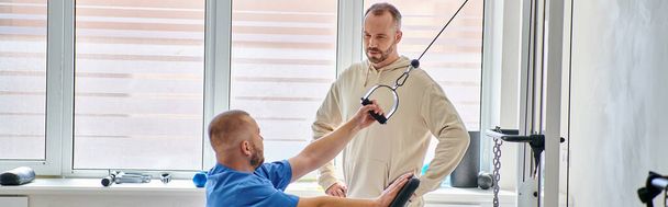 обучение молодого физиотерапевта на тренажере, инструктаж человека в центре кинезио, баннер - Фото, изображение