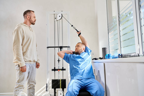 zkušený odborný výcvik na cvičební stroj během konzultace člověka v kineziologickém centru - Fotografie, Obrázek