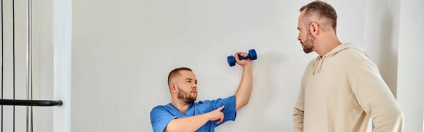 若いリハビリテーション学者 ダンベルで腕をトレーニングする方法を示す ダンベルセンターの男, バナー - 写真・画像