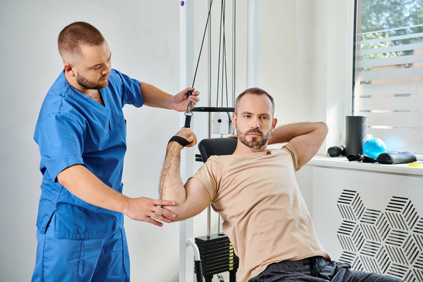 zkušený instruktor podporující muže cvičícího na cvičebním stroji v tělocvičně kinezio centra - Fotografie, Obrázek