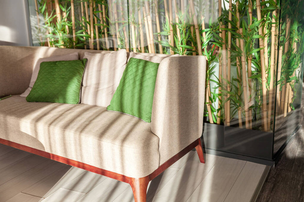Sofa mit zwei grünen Kissen auf dem Hintergrund einer Bambuswand - Foto, Bild