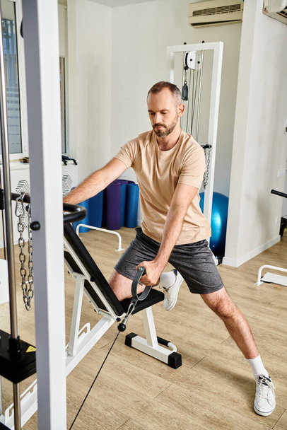 vousatý muž ve sportovním oblečení cvičit na cvičebním stroji v moderní tělocvičně kinesio centra, zotavení - Fotografie, Obrázek