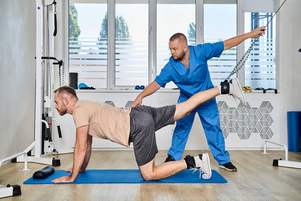 fisioterapeuta experto que ayuda al entrenamiento del hombre durante la sesión de recuperación en el gimnasio del centro kinesio - Foto, Imagen