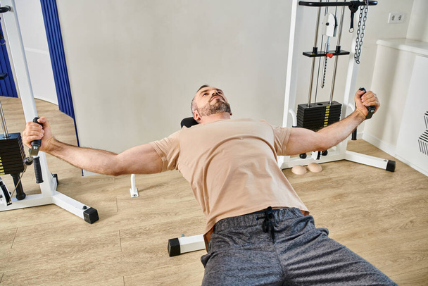 mannelijke patiënt in sportkleding uit te werken op fitnessapparaat in kinesio centrum, herstel sessie - Foto, afbeelding