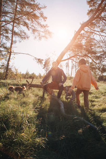 Felice giorno dei padri. Papà e figlio in una passeggiata nella foresta con il tempo soleggiato. Tempo libero in famiglia. Il padre si siede su un tronco con il figlio. Vista frontale - Foto, immagini
