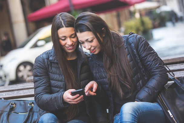 Two female twins looking at a smart phone - Foto, afbeelding