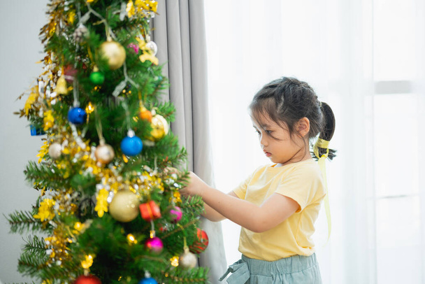 Children kids girl decorating christmas tree for celebrate christmas and new year party at home. Preparing for holiday. Happiness Christmas day. Have fun. X-mas concept. - Photo, Image