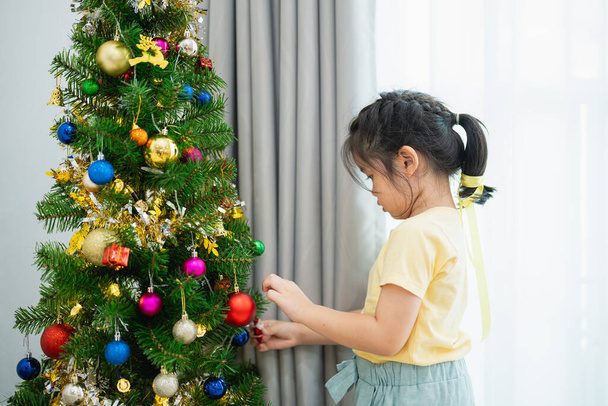 Children kids girl decorating christmas tree for celebrate christmas and new year party at home. Preparing for holiday. Happiness Christmas day. Have fun. X-mas concept. - Photo, Image