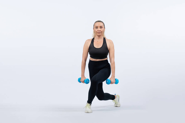 Full body length shot active and sporty senior woman lifting dumbbell during weight training workout on isolated background. Healthy active physique and body care lifestyle for pensioner. Clout - Photo, Image