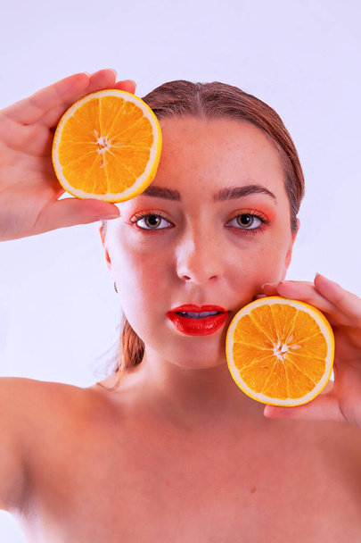 Όμορφη ξανθιά γυναίκα κρατά ένα πορτοκαλί μισό στο χέρι της με γυμνούς ώμους - Φωτογραφία, εικόνα