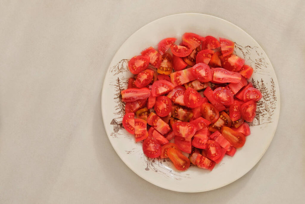 Tomaten in einem Tonteller auf beigem Hintergrund. Rote geschnittene Tomaten in rustikaler beiger Schüssel. - Foto, Bild