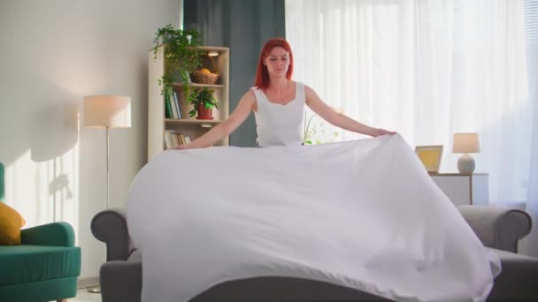 charmante huisvrouw het opmaken van haar bed na slaap in een gezellige lichte kamer - Video
